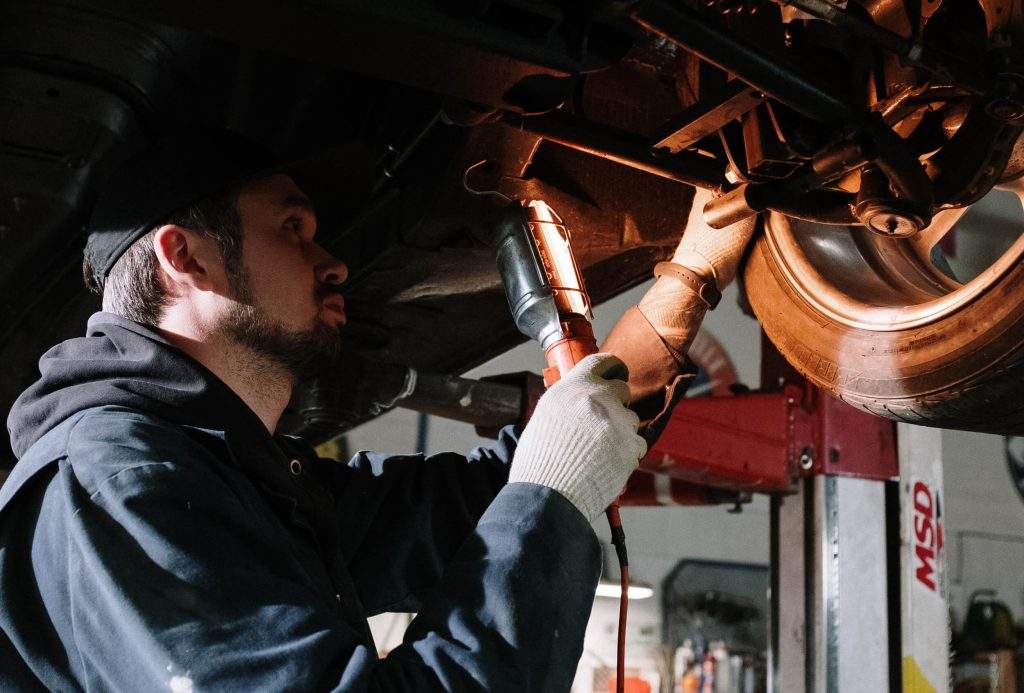 An automotive technician with a flash light looking at a vehicle's axle.