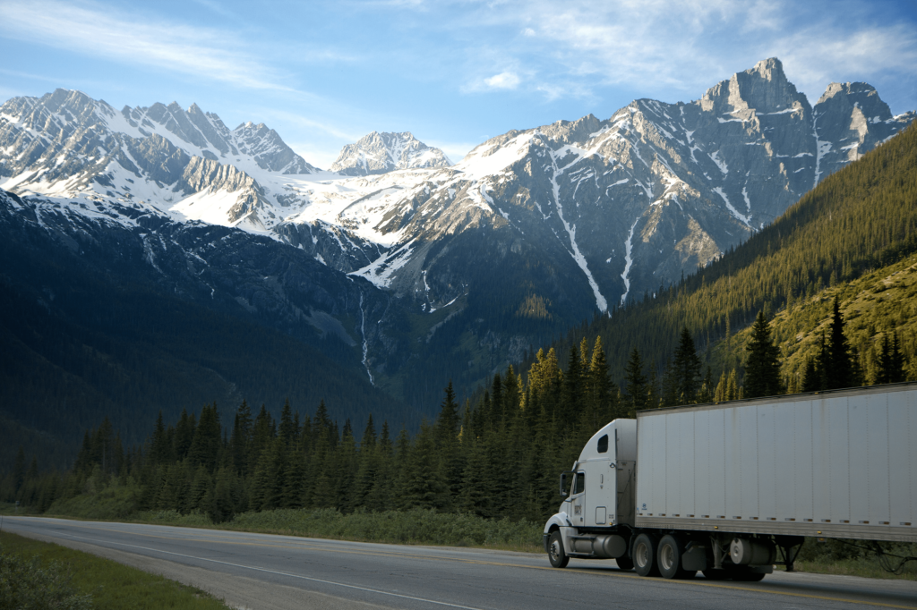 Picture of white 18 wheeler on a mountain road with mountains in the background.